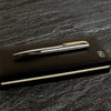 Silver pen with gold accents on a black notebook against a dark stone background