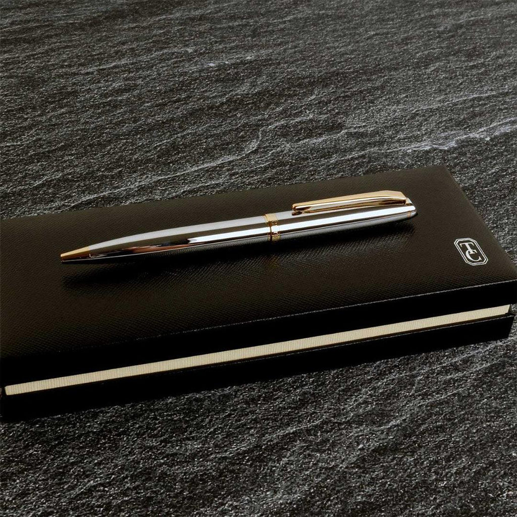 Silver pen with gold accents on a black notebook against a dark stone background